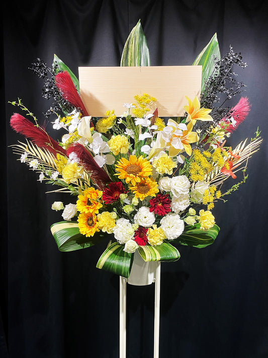 サンフラワーと赤のアクセントが映えるアーティフィシャルスタンド花(夏の公演祝いやイベントに贈る華やかな祝い花)|Re:Bloom HANA GARDEN TOKYO