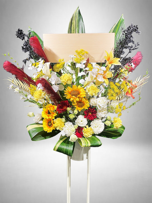 サンフラワーと赤のアクセントが映えるアーティフィシャルスタンド花(夏の公演祝いやイベントに贈る華やかな祝い花)|Re:Bloom HANA GARDEN TOKYO