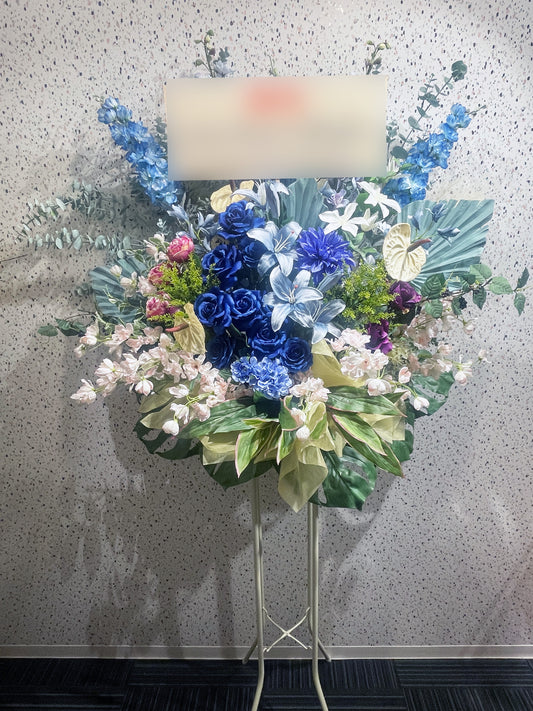 ブルーローズとユリを中心にアレンジされた、Re:Bloomシリーズのアーティフィシャルスタンド花。ライトグリーンのアンスリウムやピンクの花材がアクセントになった、涼やかで品格のあるデザイン