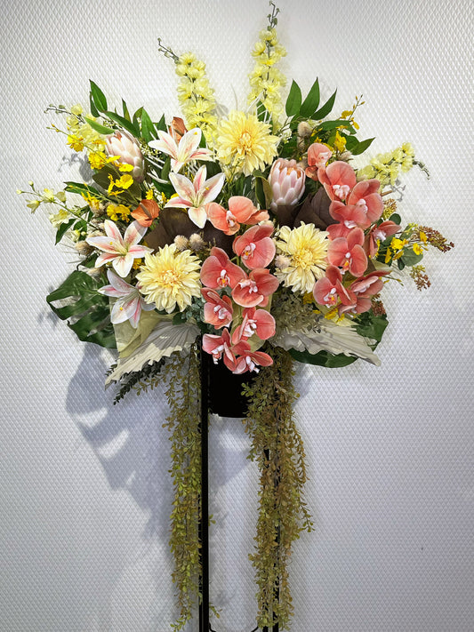 コーラルピンクの胡蝶蘭とユリを中心にしたボタニカルデザインのRe:Bloomスタンド花