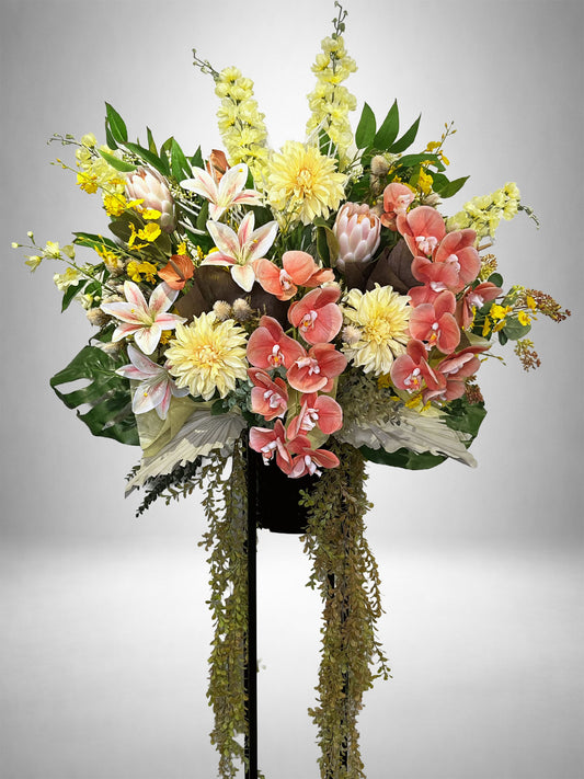 コーラルピンクの胡蝶蘭とユリを中心にしたボタニカルデザインのRe:Bloomスタンド花