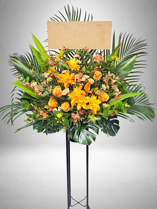 明るいオレンジの花々が太陽のように輝く、華やかでラグジュアリーなスタンド花。
リリーやローズを使用した生花デザインで、公演祝いや開店祝いに最適。