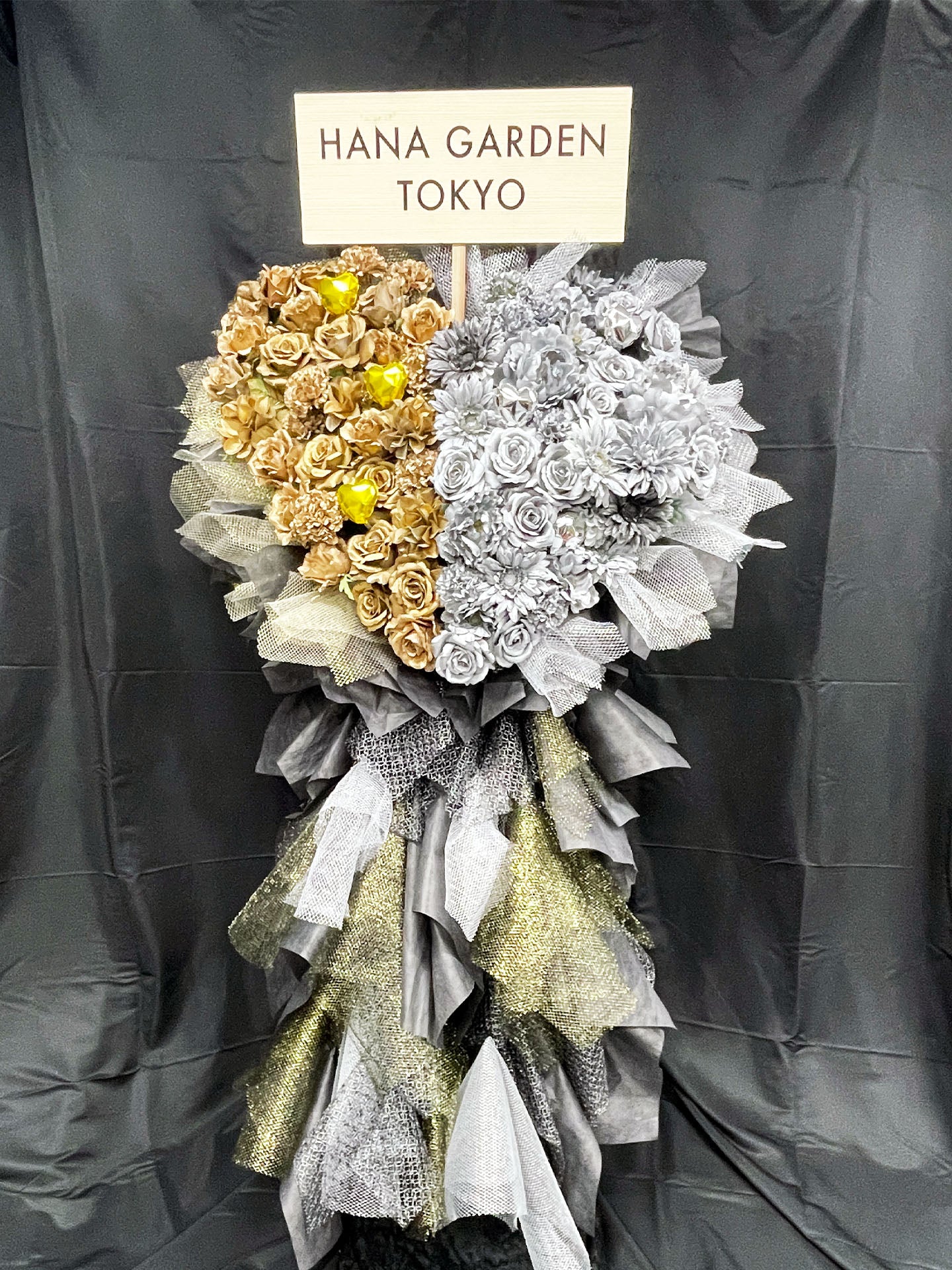 ゴールドとシルバーの2つのハートが輝くアーティフィシャルフラワースタンド。
メタリックな質感と立体感が美しく、公演祝い・周年祝い・イベント装花に最適。