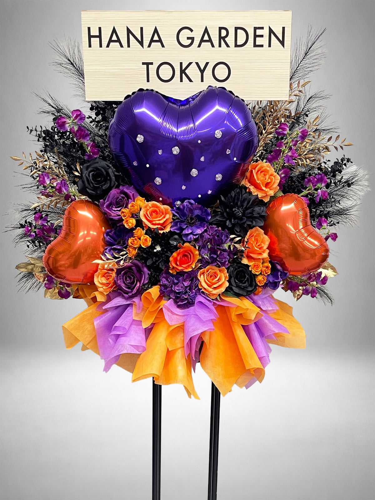 パープル・オレンジ・ブラックの花々と、大きなハート型バルーンを組み合わせた華やかなスタンド花。ライブ・公演祝い、生誕祭、誕生日、ハロウィンイベントなど、印象的で存在感のあるお祝いにおすすめです。