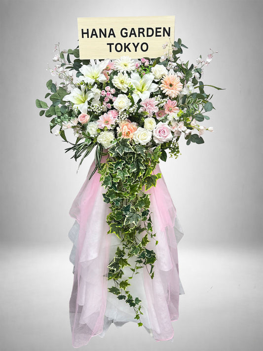 淡いピンクとホワイトの花々に、流れるグリーンを組み合わせたピンクリュミエールスタンド花。ライブ・公演祝い、生誕祭、誕生日、周年祝いなど、可愛らしく上品なお祝いにおすすめです。