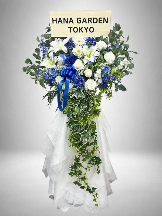 ブルーとホワイトの花々に、流れるグリーンを組み合わせたブルーリュミエールスタンド花。ライブ・公演祝い、生誕祭、誕生日、周年祝いなど、ブルーをテーマにした爽やかで華やかなお祝いにおすすめです。